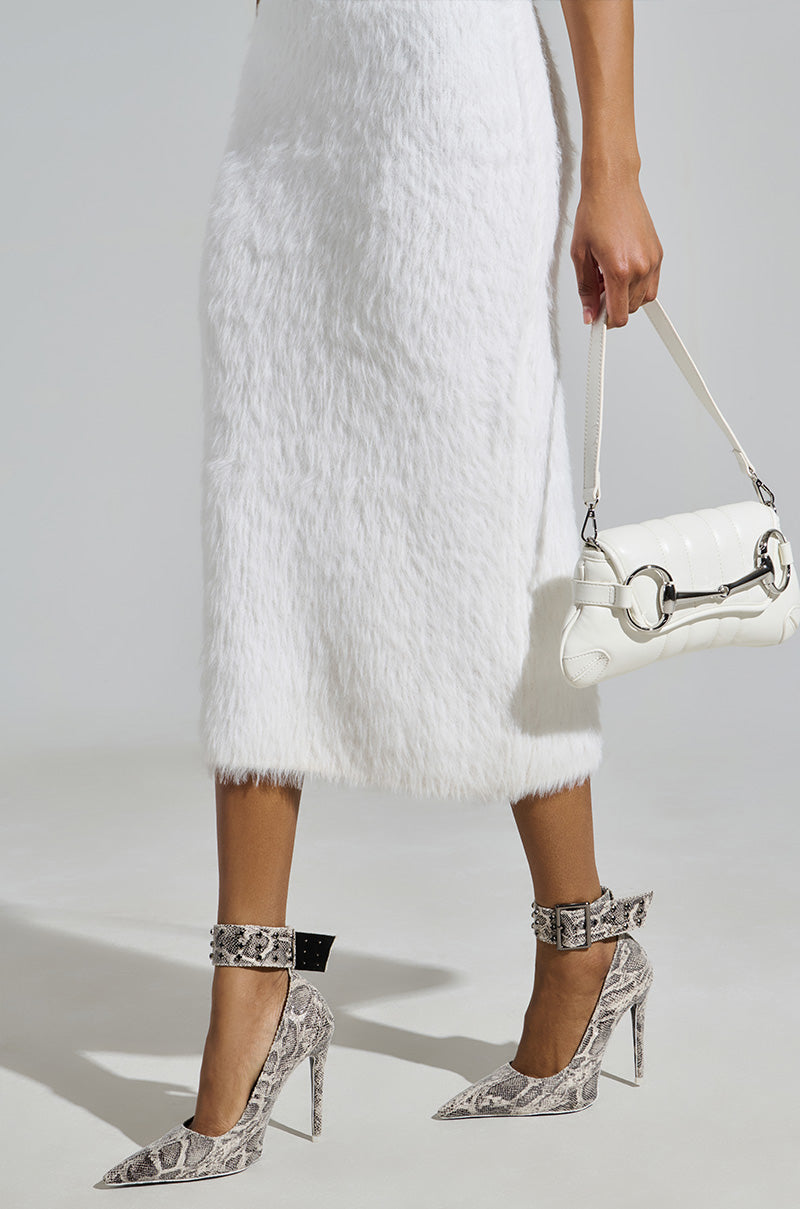 A person wearing a white fuzzy midi dress, AZALEA WANG VOLNEY SNAKE STILETTO PUMPS with an embossed snakeskin pattern, and holding a white handbag with a silver chain strap. The neutral background highlights the outfit's textures and patterns.
