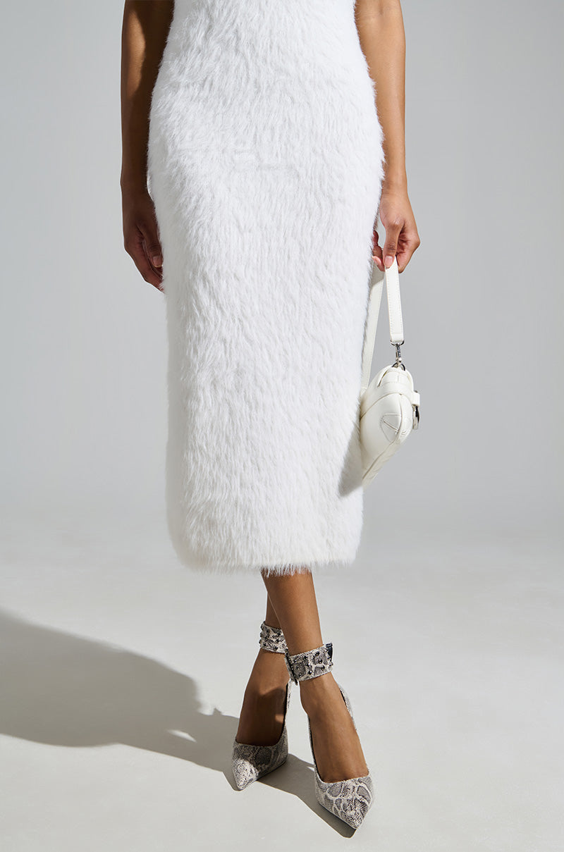 A person in a white fuzzy dress and carrying a white handbag stands against a gray background. Their feet dazzle in AZALEA WANG Volney Snake Stiletto Pumps, featuring an embossed snakeskin pattern that perfectly complements the ensemble's elegance.