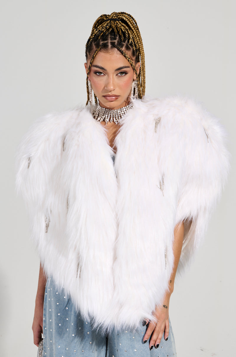 A person with braided hair and bold makeup flaunts the LIMITED EDITION STAR LOVER FAUX FUR HEART VEST IN WHITE along with a sparkling choker. The vest perfectly complements a denim outfit dazzling with rhinestone embellishments, while the plain background highlights their stylish ensemble.