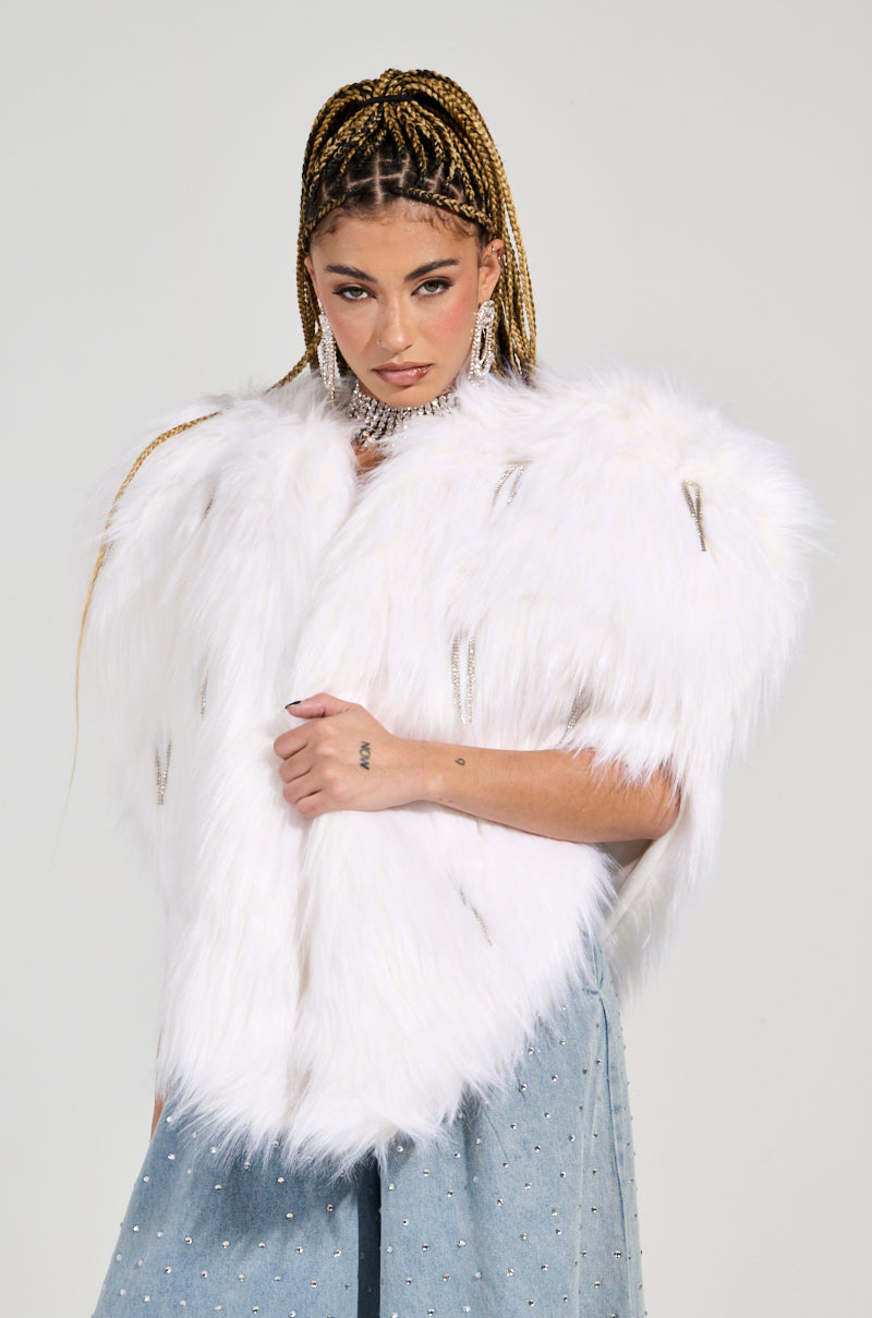 A person with braided hair is wearing a standout piece: the Limited Edition Star Lover Faux Fur Heart Vest in White paired with a rhinestone-embellished denim skirt. They sport large hoop earrings and a silver choker necklace, all set against a plain, light-colored background.