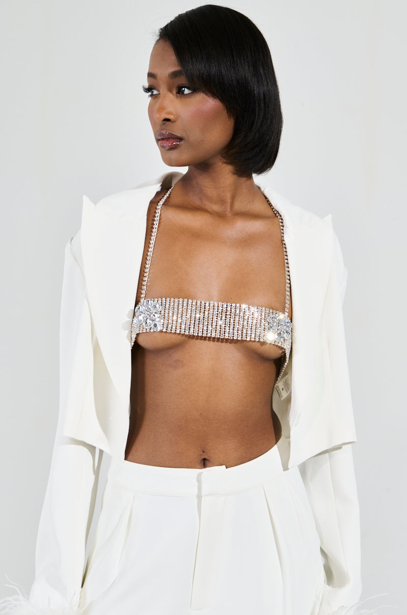 A person with short black hair is wearing a white jacket over a sparkling embellished top, adorned with the STAR GURL BLING BODY CHAIN. The outfit includes white pants, perfectly complemented by silver jewels against a plain and light-colored background.