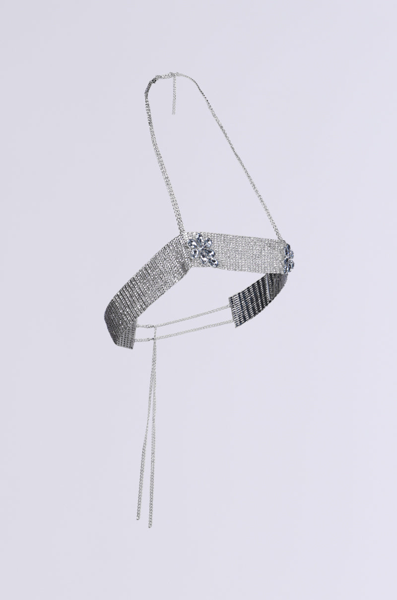 The STAR GURL BLING BODY CHAIN features a silver metallic design with intricate floral accents and delicate hanging chains, enhanced by silver jewels on a plain gray background, creating a mesmerizing rhinestone link base.