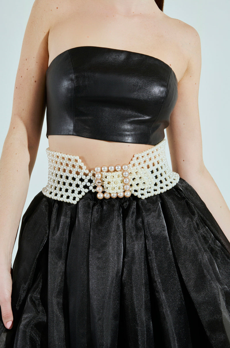 Sporting the PEARL PLEASE BELT, a black leather strapless top, and a textured black skirt, the ensemble boasts an ornate design with pearl beads and a striking buckle. The light neutral background highlights the overall elegance. 1