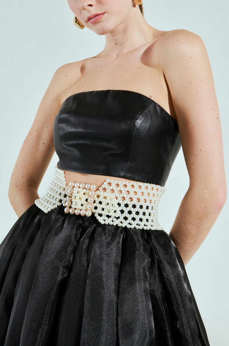 A woman wears a strapless black leather top and a satin skirt, highlighted by the PEARL PLEASE BELT. Her short hair frames her as the image focuses on her upper body and cinched waist for an elegant look.