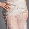 Wearing a sheer white lace dress with intricate patterns, the model showcases the STAY DRIPPIN PEARL BELT—an eye-catching faux pearl and bead statement piece draped at the waist. One hand rests on her hip; image is cropped at the torso.