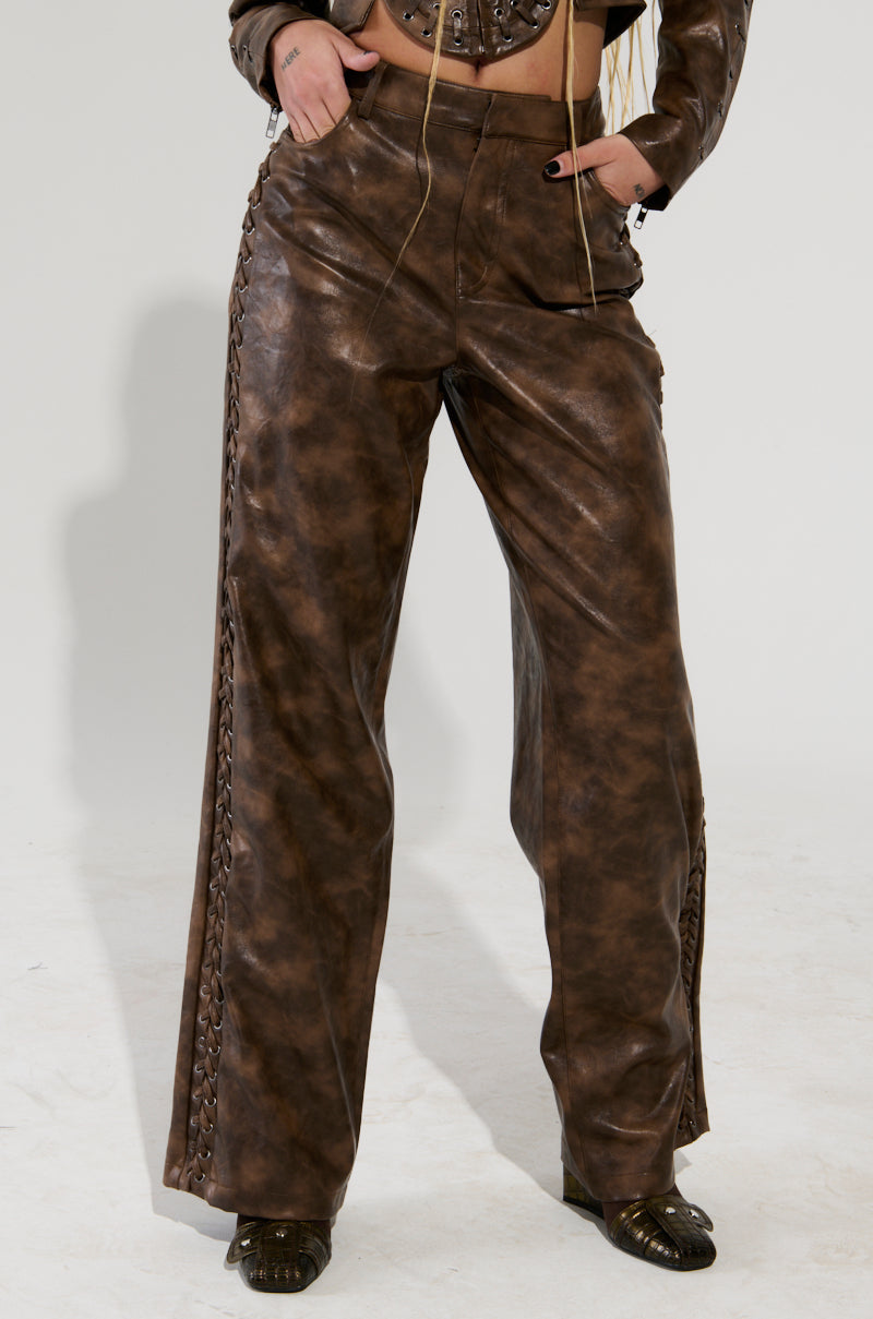 A person wearing AKIRA Label's UP TO IT LACE UP TROUSERS stands on a light floor, paired with dark shoes that feature a textured design.