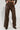 A person wearing AKIRA Label's UP TO IT LACE UP TROUSERS stands on a light floor, paired with dark shoes that feature a textured design.