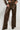 The individual sports the chic UP TO IT LACE UP TROUSERS, which are high-waisted and made of faux leather, featuring intricate lace-up details along the sides. These pants have a marbled texture that stands out against the light background and are paired with a matching AKIRA Label jacket.