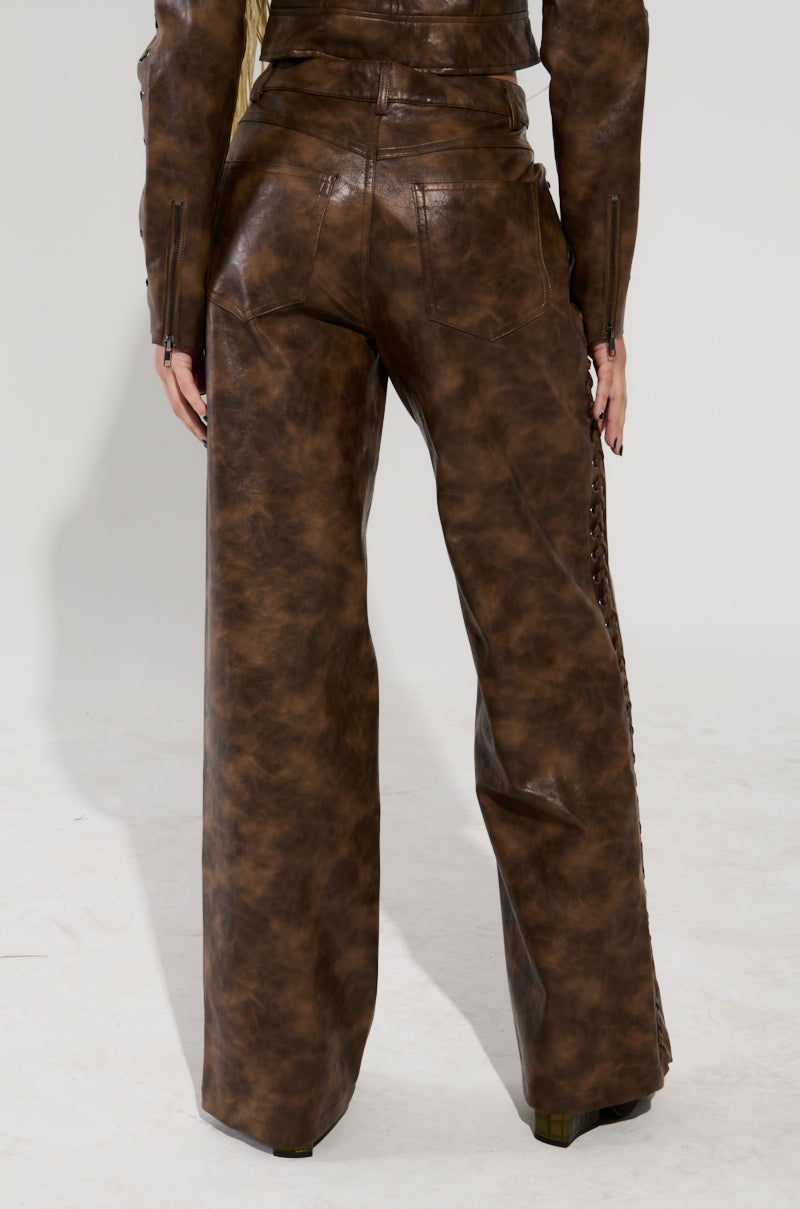 A person is seen from behind wearing the UP TO IT LACE UP TROUSERS, designed in brown faux leather with laced-up detailing on the sides. They are paired with a matching AKIRA Label jacket, and the wide-leg style of the trousers is highlighted against a plain white backdrop.