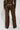 A person is seen from behind wearing the UP TO IT LACE UP TROUSERS, designed in brown faux leather with laced-up detailing on the sides. They are paired with a matching AKIRA Label jacket, and the wide-leg style of the trousers is highlighted against a plain white backdrop.