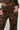 A person dressed in a chic, faux leather outfit from the AKIRA Label, featuring intricate lace-up details on the UP TO IT LACE UP TROUSERS and matching jacket. With their hands resting in pockets, black painted nails catch the eye alongside a tattoo reading 