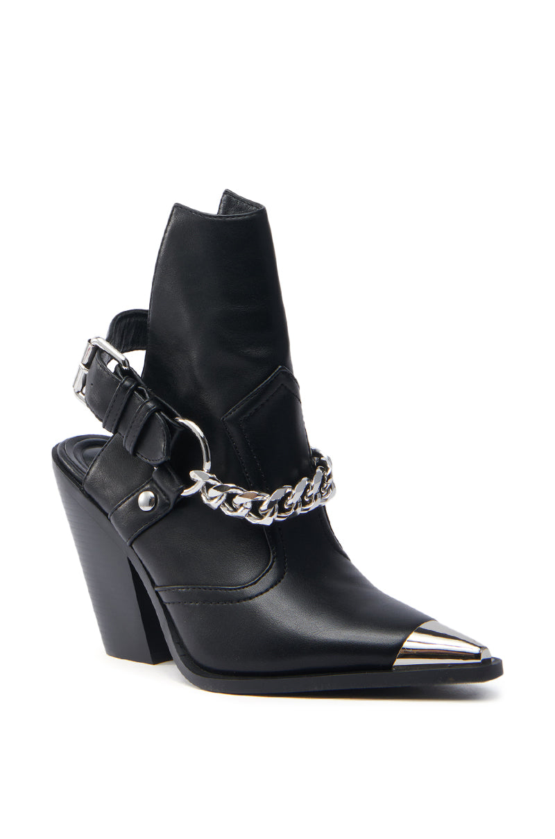 The AZALEA WANG WADE BLACK WESTERN BOOTIE is a black high-heeled ankle boot made from vegan leather, featuring a pointed metal toe, decorative silver chain across the front, cutout heel design, and buckle strap for a structured modern silhouette.