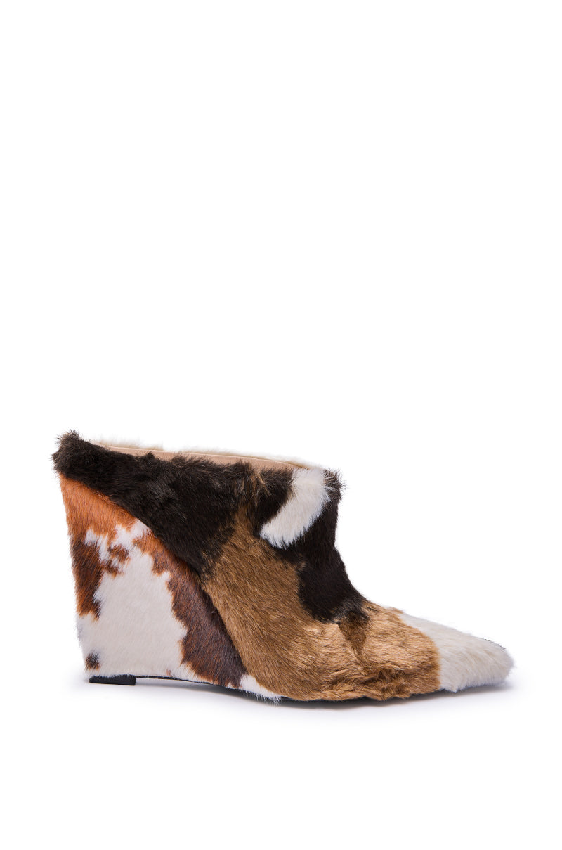 The AZALEA WANG WAFIYA MULTI WEDGE COW PATTERN FURRY PUMP is a wedge-heeled shoe with a pointed toe, covered in multicolored faux fur in brown, white, and black cow patterns for a bold, sculptural look.