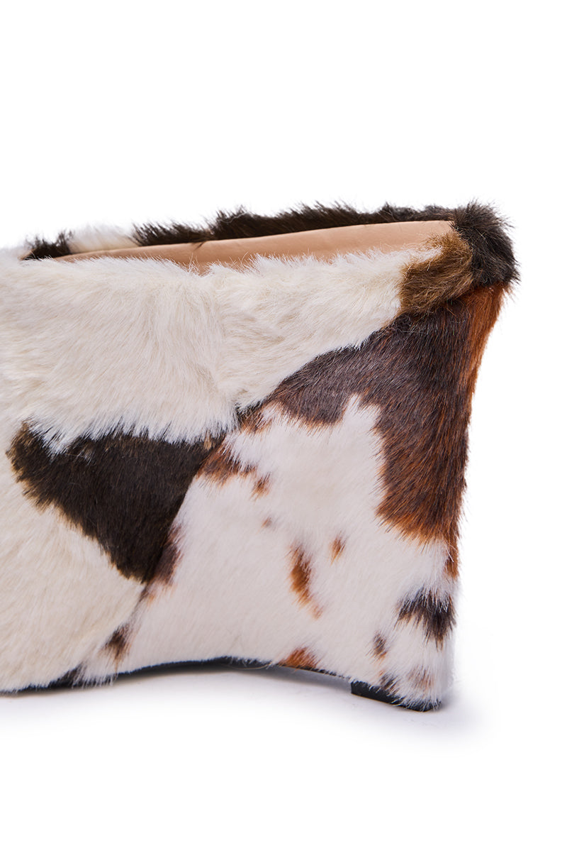 A close-up of a rectangular clutch purse in multicolored cowhide fur echoes the playful style of the AZALEA WANG WAFIYA MULTI WEDGE COW PATTERN FURRY PUMP, with brown, black, and white patches on a white background.