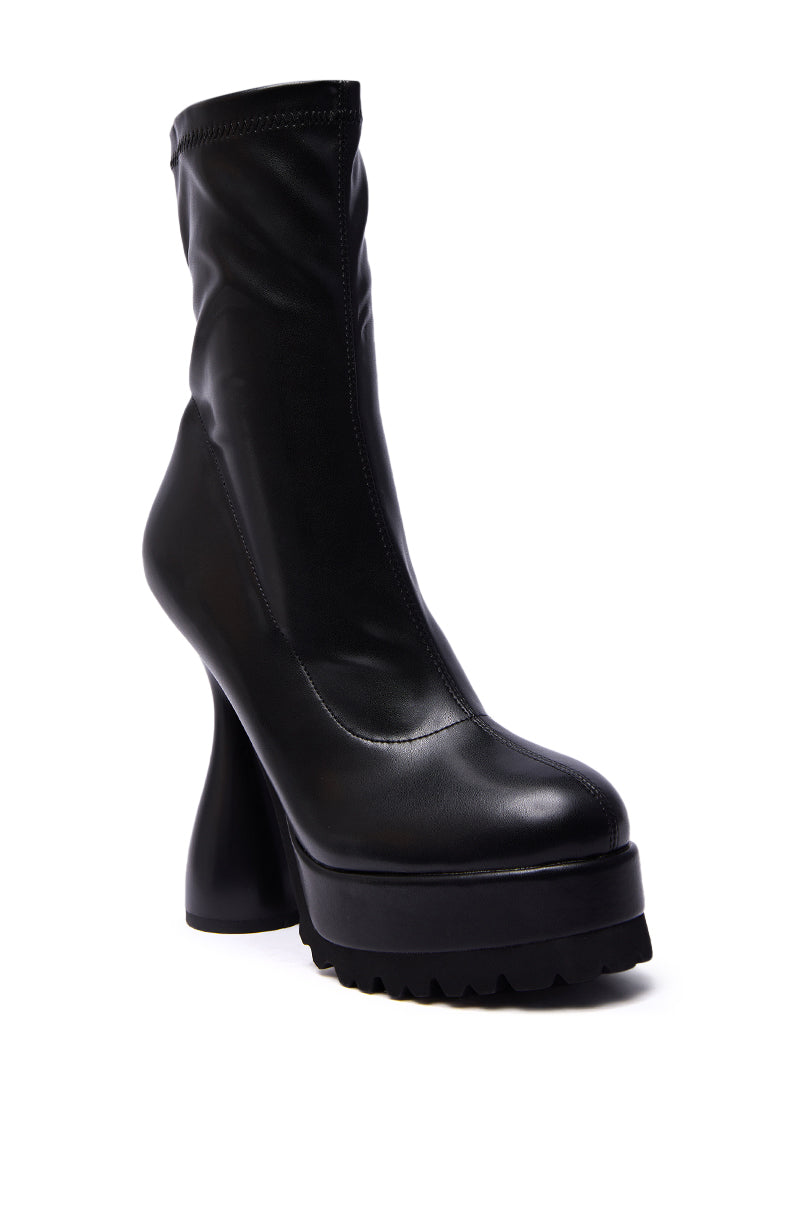 The AZALEA WANG WARIO BLACK CHUNKY BOOTIE features a sculpted heel and thick ridged platform sole, crafted from smooth, shiny faux leather for a bold yet polished look.