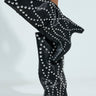 Someone is wearing the AZALEA WANG WELLS BLACK EMBELLISHED BOOT, knee-high in vegan leather with silver studs and a slight heel, covering much of the legs against a light background.