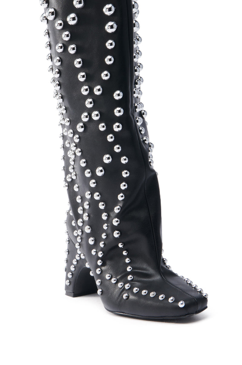 The AZALEA WANG WELLS BLACK EMBELLISHED BOOT is a black knee-high boot made from vegan leather, adorned with silver studs in swirling patterns. It features a square toe and a chunky heel.