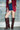 A person in a burgundy blazer, white top, denim shorts, and the AZALEA WANG WELLS NEW BURGUNDY CROC BOOT stands before a glass block wall.