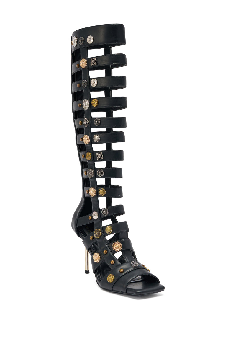 The AZALWA WANG Gold Wentworth Gladiator sandal is a black, knee-high, open toe style featuring multiple horizontal straps, a thin high heel, two toned hardware, metallic studs and decorative buttons along the front. 3