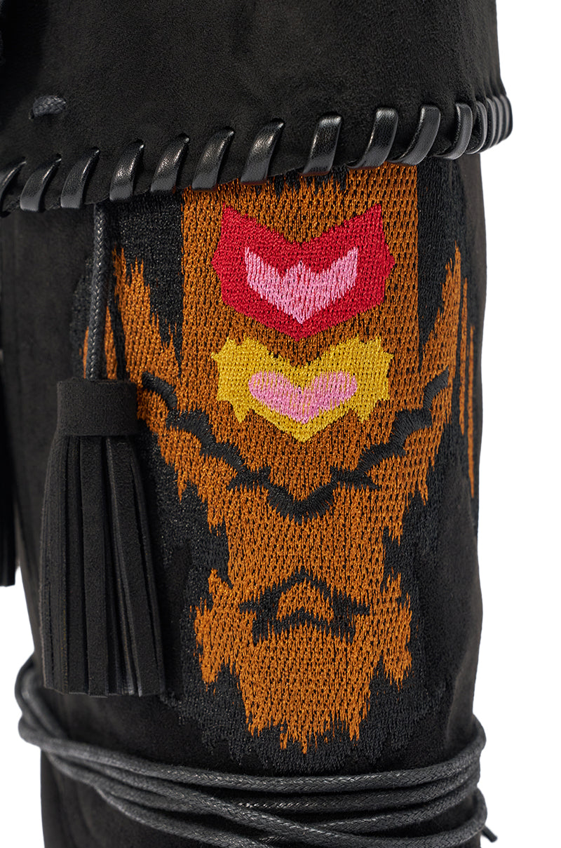 Close-up of the AZALEA WANG WERET BLACK FLAT BOOTIE in faux suede, featuring thick braided trim, black leather tassels, and detailed orange, red, yellow, and pink embroidered geometric patterns.