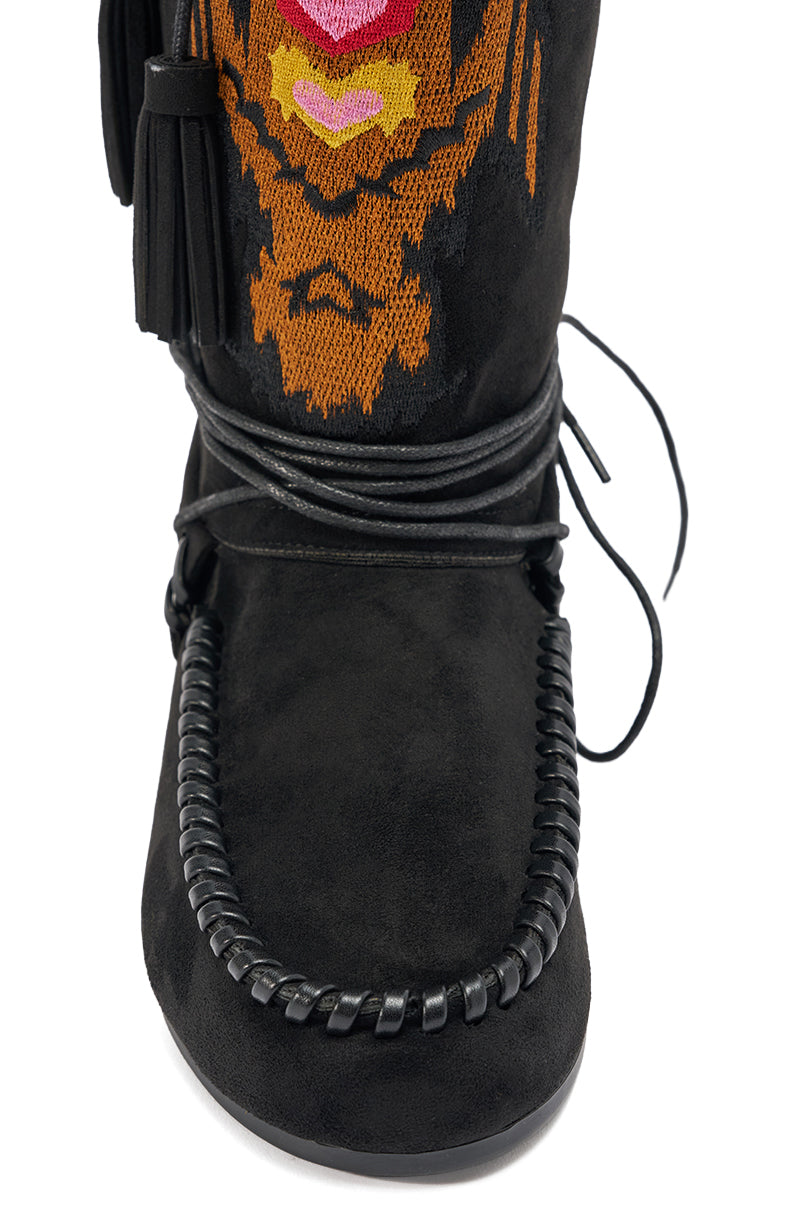 Close-up of the AZALEA WANG WERET BLACK FLAT BOOTIE, a black faux suede moccasin-style bootie with braided trim, decorative leather laces, and orange, pink, and yellow embroidery on the upper front.