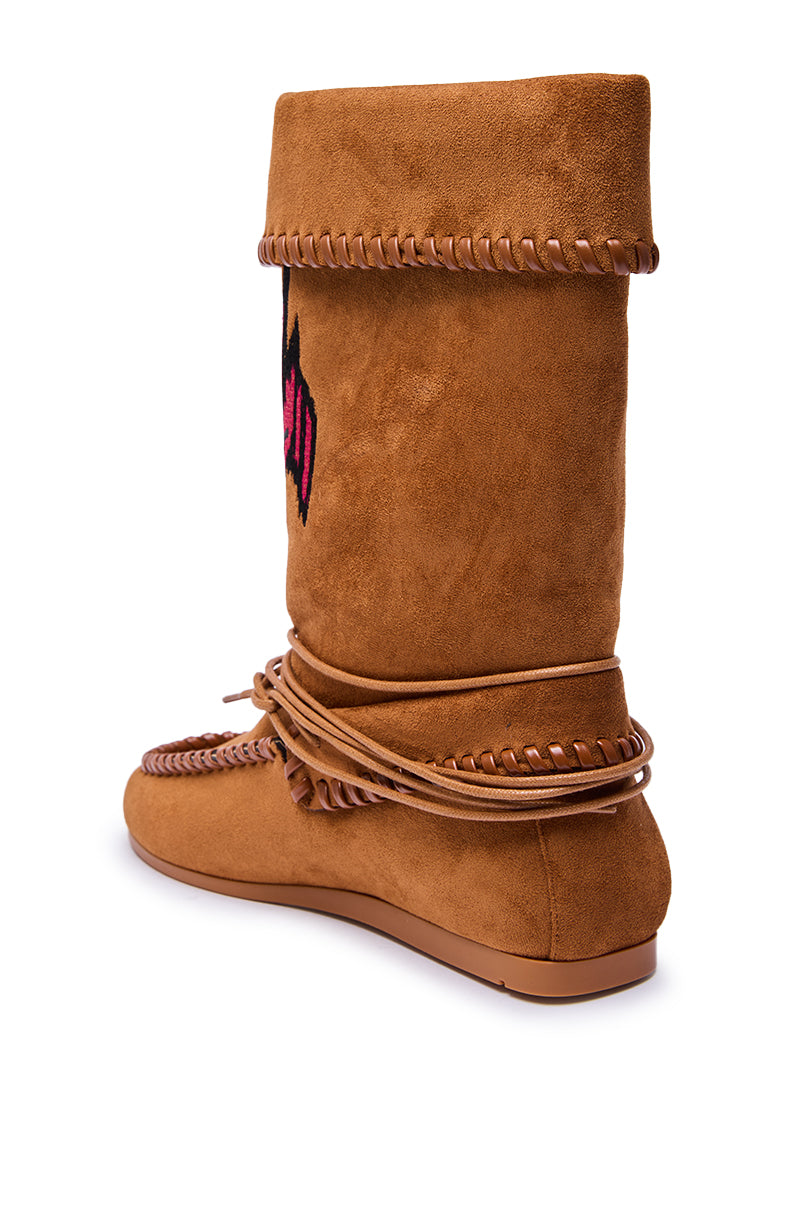 The AZALEA WANG WERET CHESTNUT FLAT BOOTIE is a brown faux suede moccasin-style boot with braided trim, decorative stitching, fold-over top, wrap-around laces, and a small red and black side design.