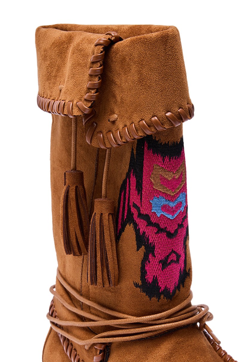 A close-up of the AZALEA WANG WERET CHESTNUT FLAT BOOTIE in brown faux suede highlights leather lacing, tassels, decorative stitching, and colorful pink, blue, and black geometric embroidery on the upper.