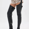 Wearing the AZALEA WANG WESTLANN BLACK PU CHAP BOOT—black, Western-inspired thigh-high faux leather boots with side zippers and pointed toes—paired with animal print shorts and a black belt, against a plain white background.