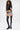A woman with curly hair wears a black sleeveless crop top, leopard print faux leather shorts with a belt, and AZALEA WANG WESTLANN BLACK PU CHAP BOOTs. She stands facing forward against a plain white background.