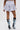 A person stands facing away, wearing the HEATHERED BUBBLE SHORT in light gray cotton with a high-rise fit and two-tone denim high-heeled boots featuring white laces, set against a plain white background.