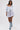 A woman models the HEATHERED BUBBLE SHORT, a high-rise gray ruffled mini skirt, paired with a light blue off-shoulder denim jacket and lace-up denim boots, walking confidently against a plain white background.