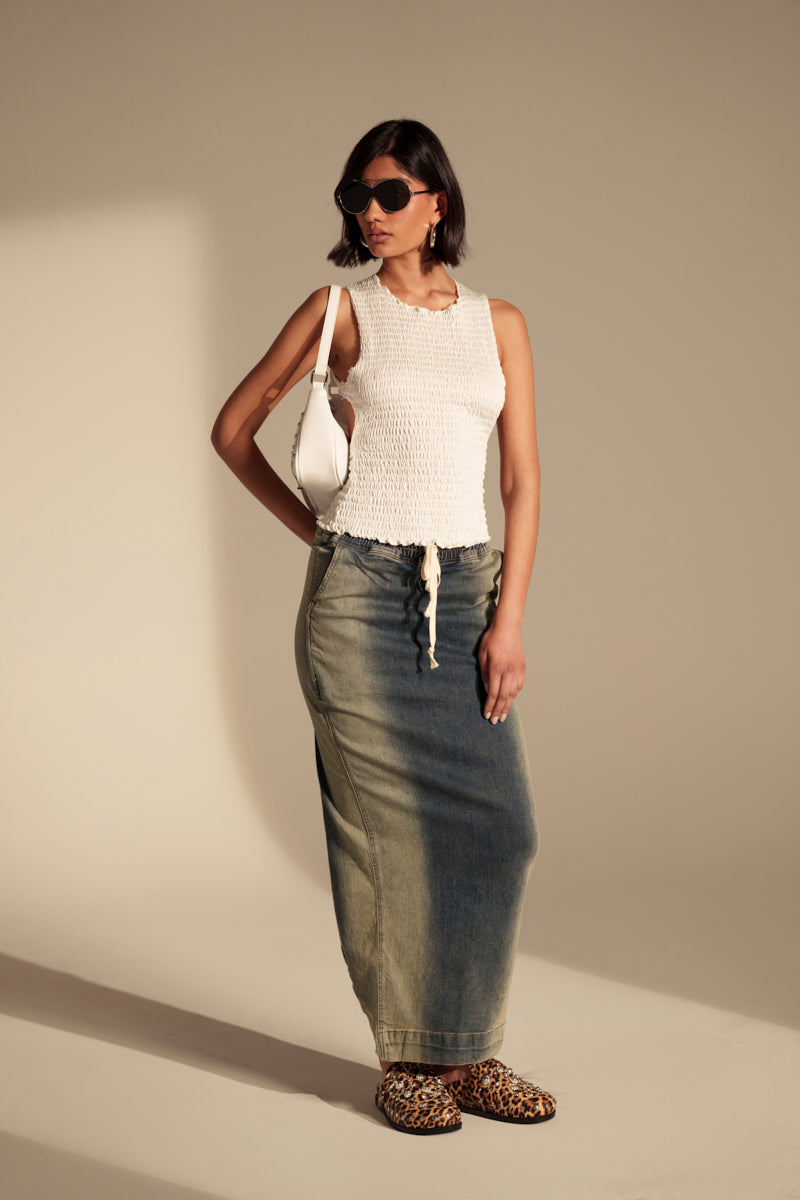 A woman in sunglasses, a white sleeveless top, the SIDE THOUGHTS MAXI SKIRT, leopard print shoes, and a white handbag poses against a neutral background.