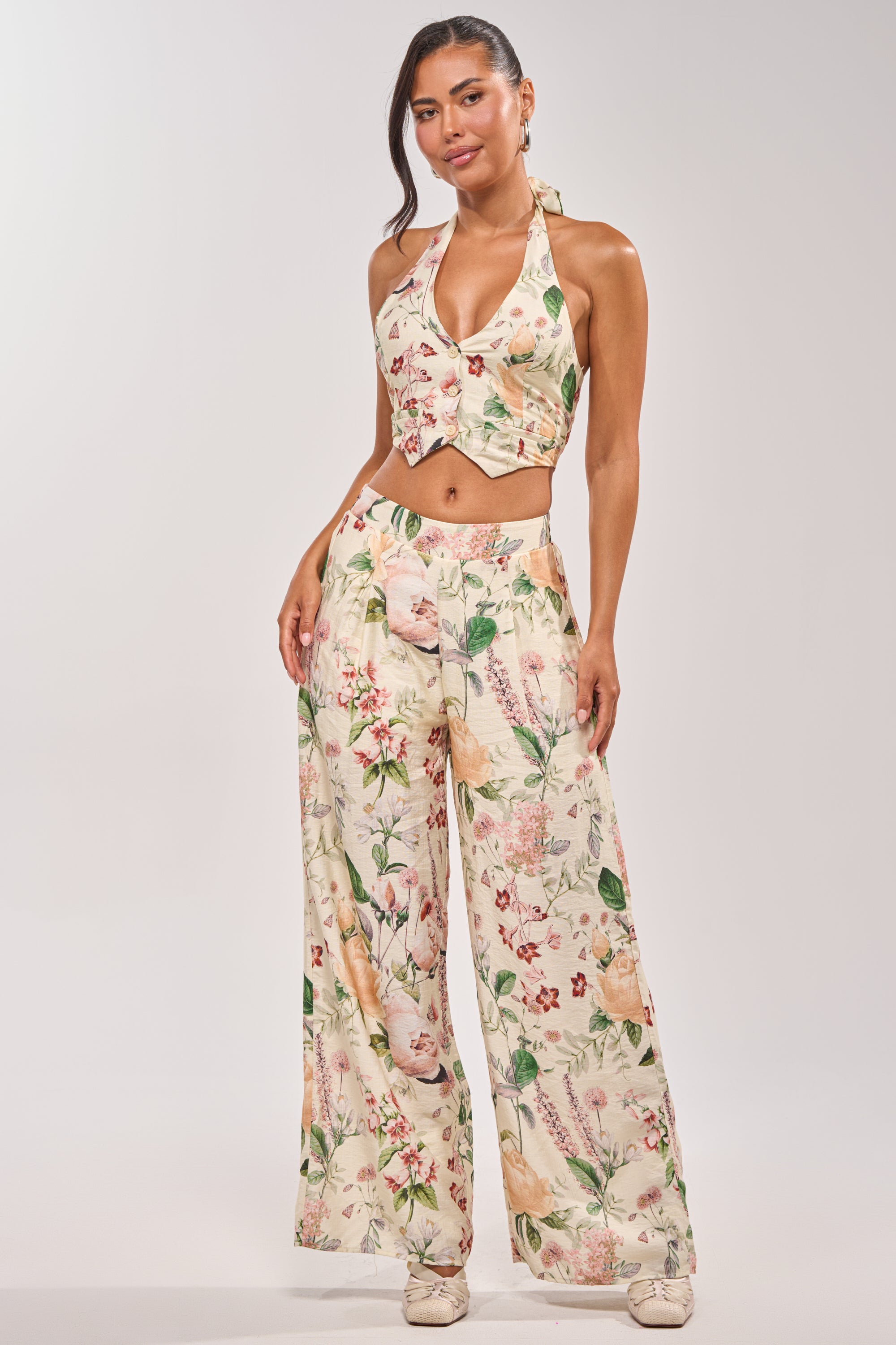 A woman stands confidently in the LADY B BUTTON DOWN TANK—cream floral print, halter style—paired with matching wide-leg cut-out pants and cream platform shoes, set against a plain light background. 5