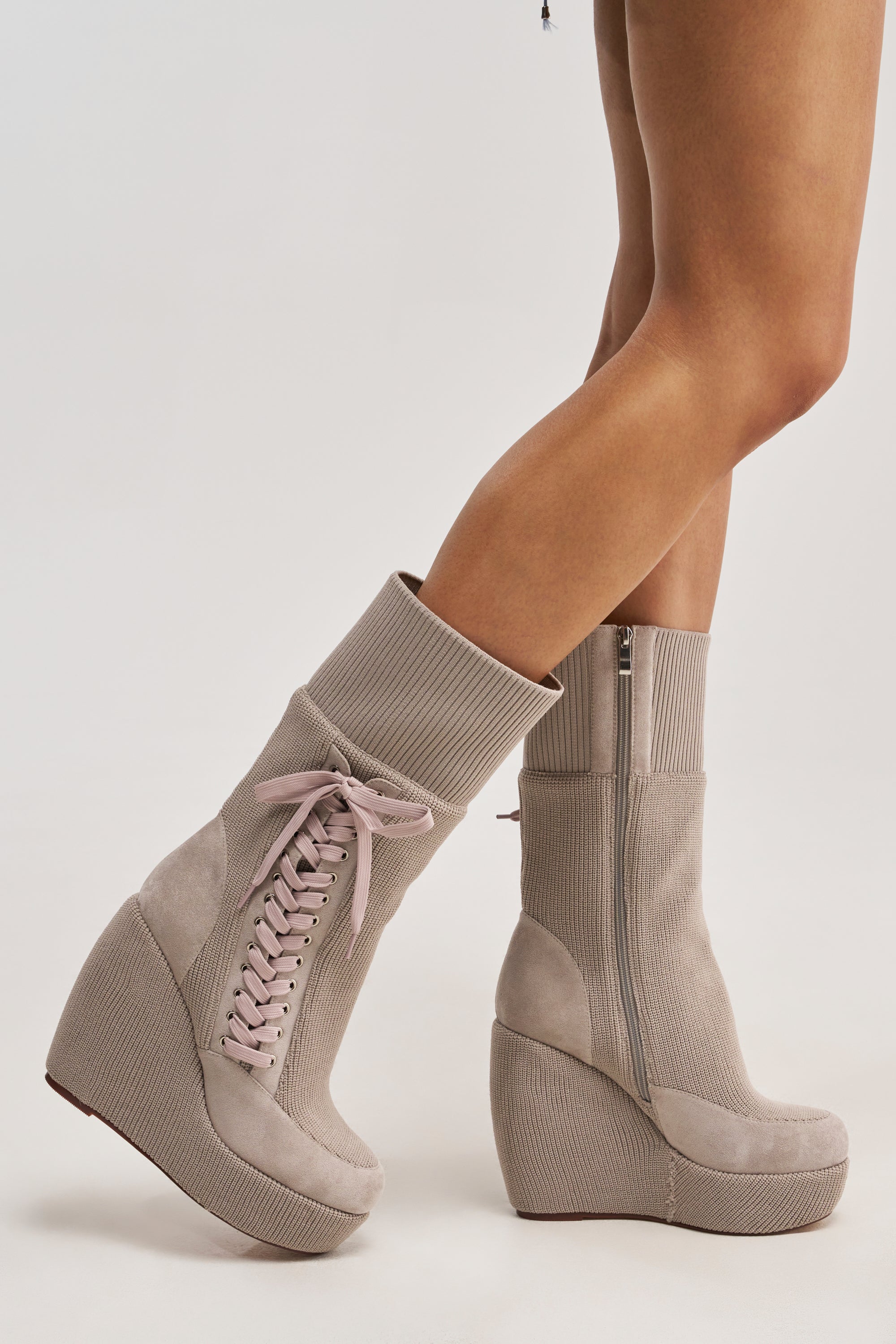 Someone stands on light flooring wearing the AKIRA GOLD WHATEVER WARM GREY CANVAS WEDGE BOOTIE, featuring pink laces, ribbed texture, and a side zipper—ideal cold weather boots for a chic and cozy look.