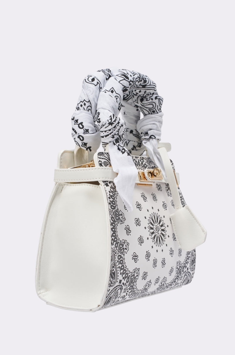 The VIVIENNE PAISLEY PRINT BAG, a white faux leather handbag with black paisley patterns, gold clasp, and a white bandana-style scarf on the handle, is shown angled against a plain light background. 2