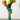 A person wearing a vivid green fuzzy sweater and the AZALEA WANG Wilber Bootie with stretch neoprene, featuring metallic stiletto heels, is captured mid-step while lifting one leg. The plain white wall in the background and the neutral-toned flooring complement the scene.