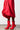 A person wearing a flowing red skirt and the AZALEA WANG WILBER BOOTIE WITH STRETCH NEOPRENE IN RED. The minimalistic background highlights the vibrant color and stylish design of the clothing and stiletto heels.