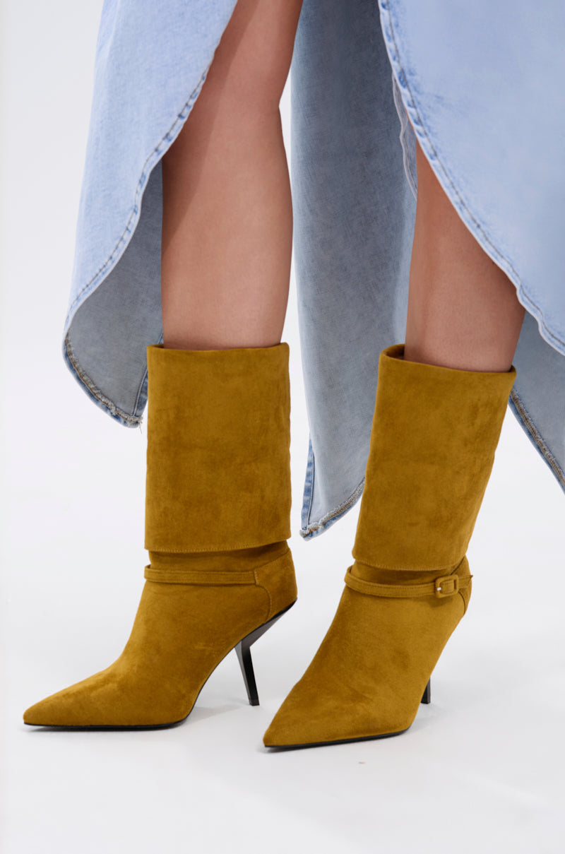 Close-up of a person wearing the AZALEA WANG WINDING OLIVE STILETTO BOOTIE with pointed toes, faux suede upper, and ankle straps, paired with a light blue denim skirt with an uneven hem against a plain white background.