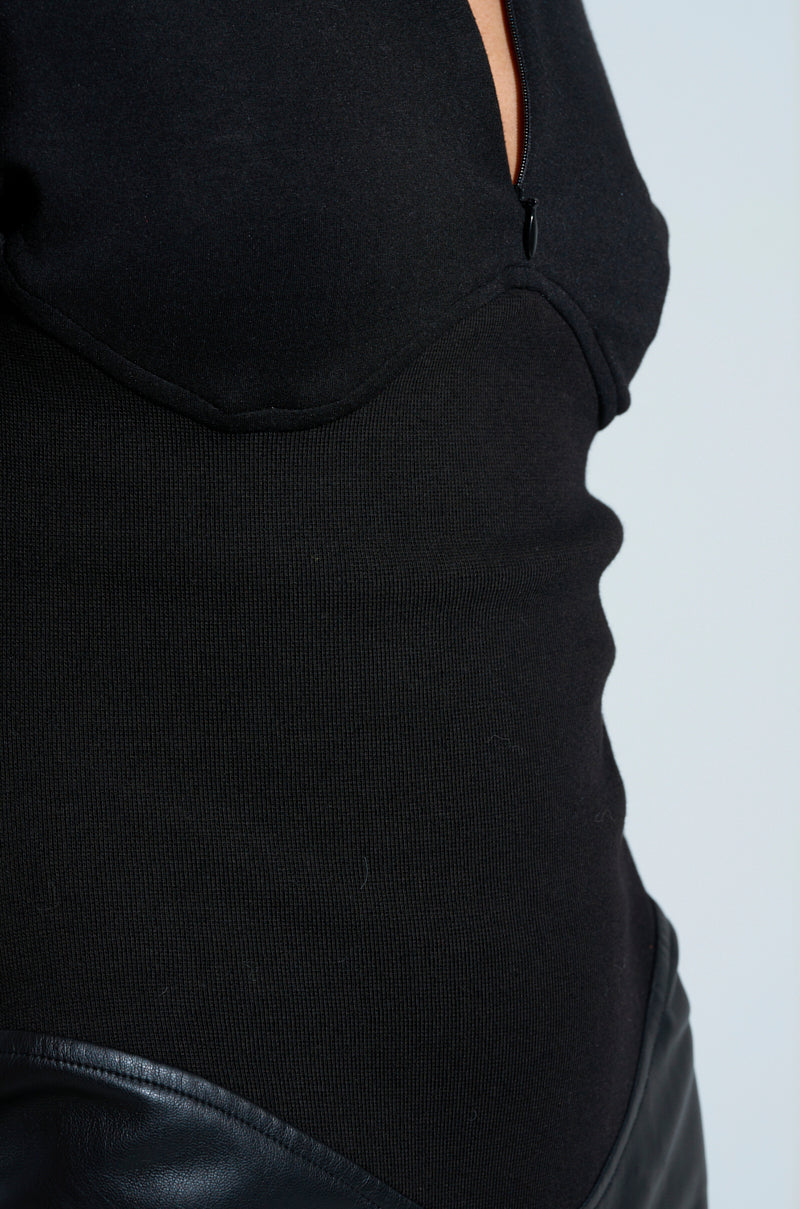 A person is dressed in a fitted black top paired with sleek faux leather pants. The image emphasizes the midsection, showcasing the texture and contrast between the fabric of the top and the leather material, reminiscent of wearing a stylish CHARLI STACKED PU JUMPSUIT IN BLACK.
