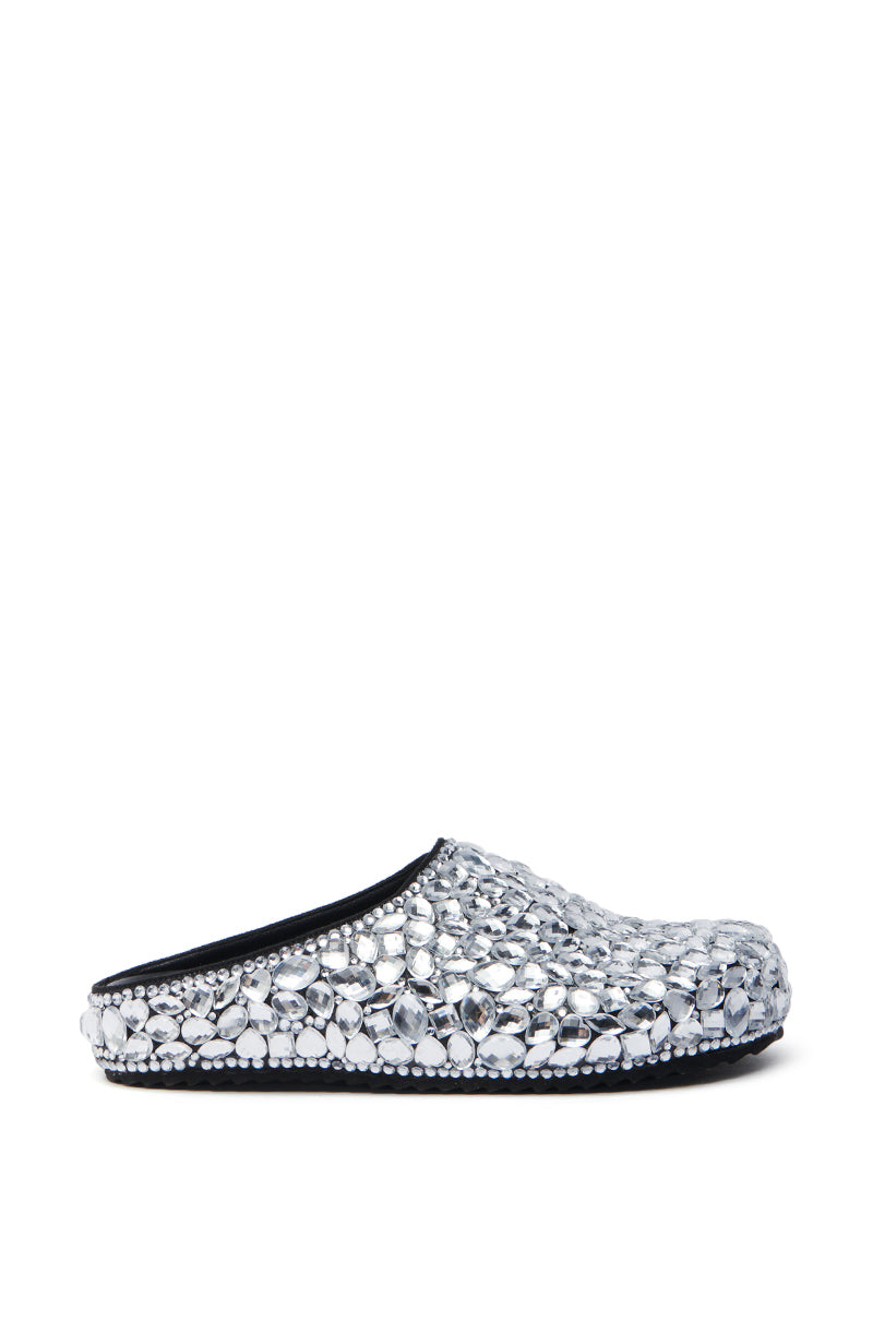 The AZALEA WANG WORLDCLASS EMBELLISHED SLIDE is a stunning silver slip-on adorned with sparkling gemstones, creating a textured surface. It features sleek black faux leather lining and sole, beautifully displayed on a white background.