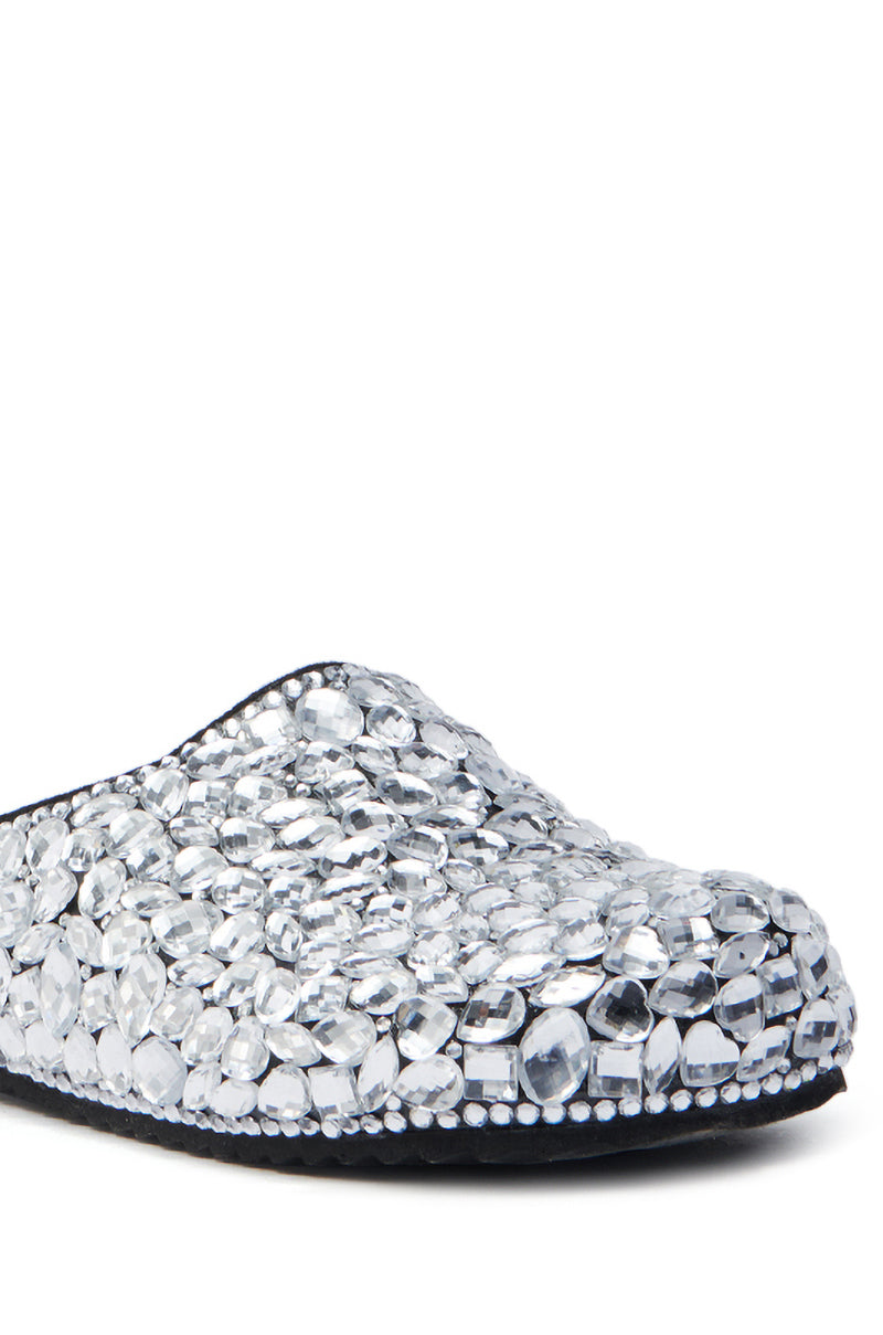 A close-up of the AZALEA WANG WORLDCLASS EMBELLISHED SLIDE reveals it covered in large, shiny, silver rhinestones. The faux leather shoe with a black sole is adorned with glittering gemstones, creating an elegant and luxurious sparkling effect.