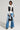 A fashionable individual stands confidently in the GET TO IT DENIM PANT paired with a stylish white jacket featuring black accents. They carry a small black handbag and wear pointed shoes, which highlight the wide-leg silhouette of their ensemble. The simple light gray background enhances the modernity of their outfit.