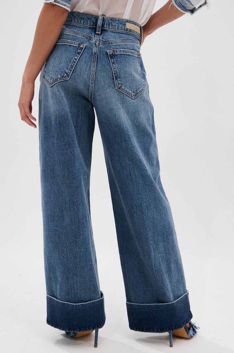 Person wearing JORDAN WIDE LEG DENIM—high-rise, wide-leg blue jeans with cuffed hems and back pockets—photographed from behind against a plain light background, highlighting the classic wide-leg silhouette.