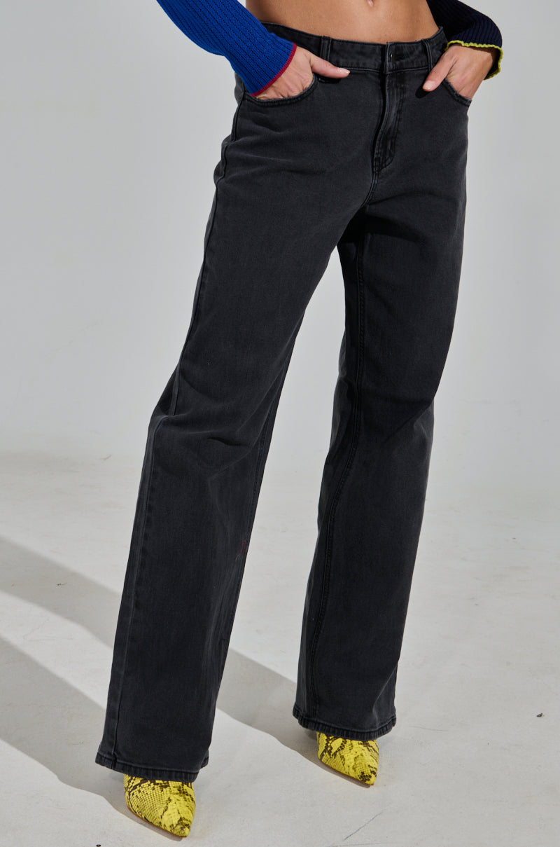 A person is wearing Nicole Vintage Low Rise Jeans in black, paired with bright yellow snake print heeled boots and a blue top. Only their lower torso and legs are visible against a plain light grey background.