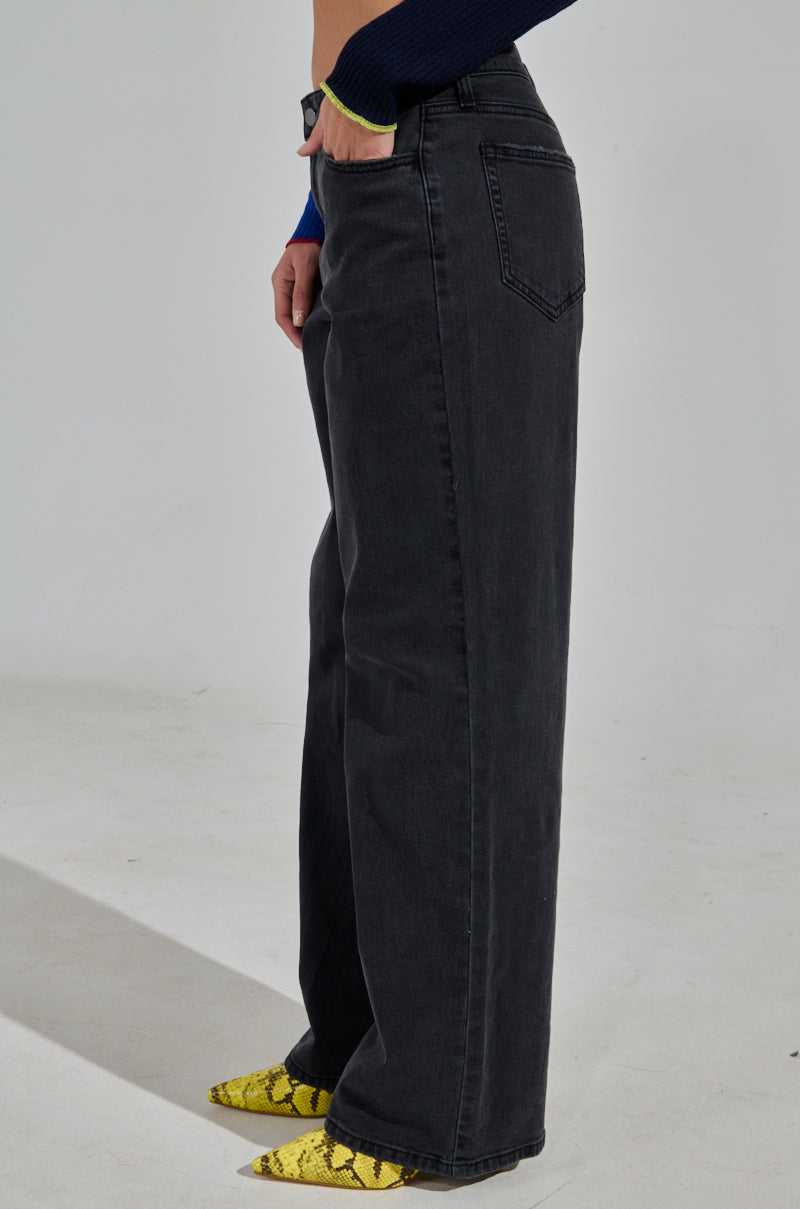 Person wearing NICOLE VINTAGE LOW RISE JEAN in black and a navy sweater, standing sideways. Their shoes are yellow with black snake patterns.
