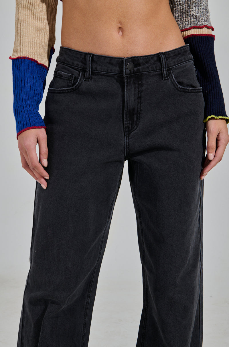 A person is wearing the NICOLE VINTAGE LOW RISE JEAN paired with a color-block sweater featuring blue, red, beige, and gray panels. The view focuses on the jeans and sweater details against a plain light gray background.