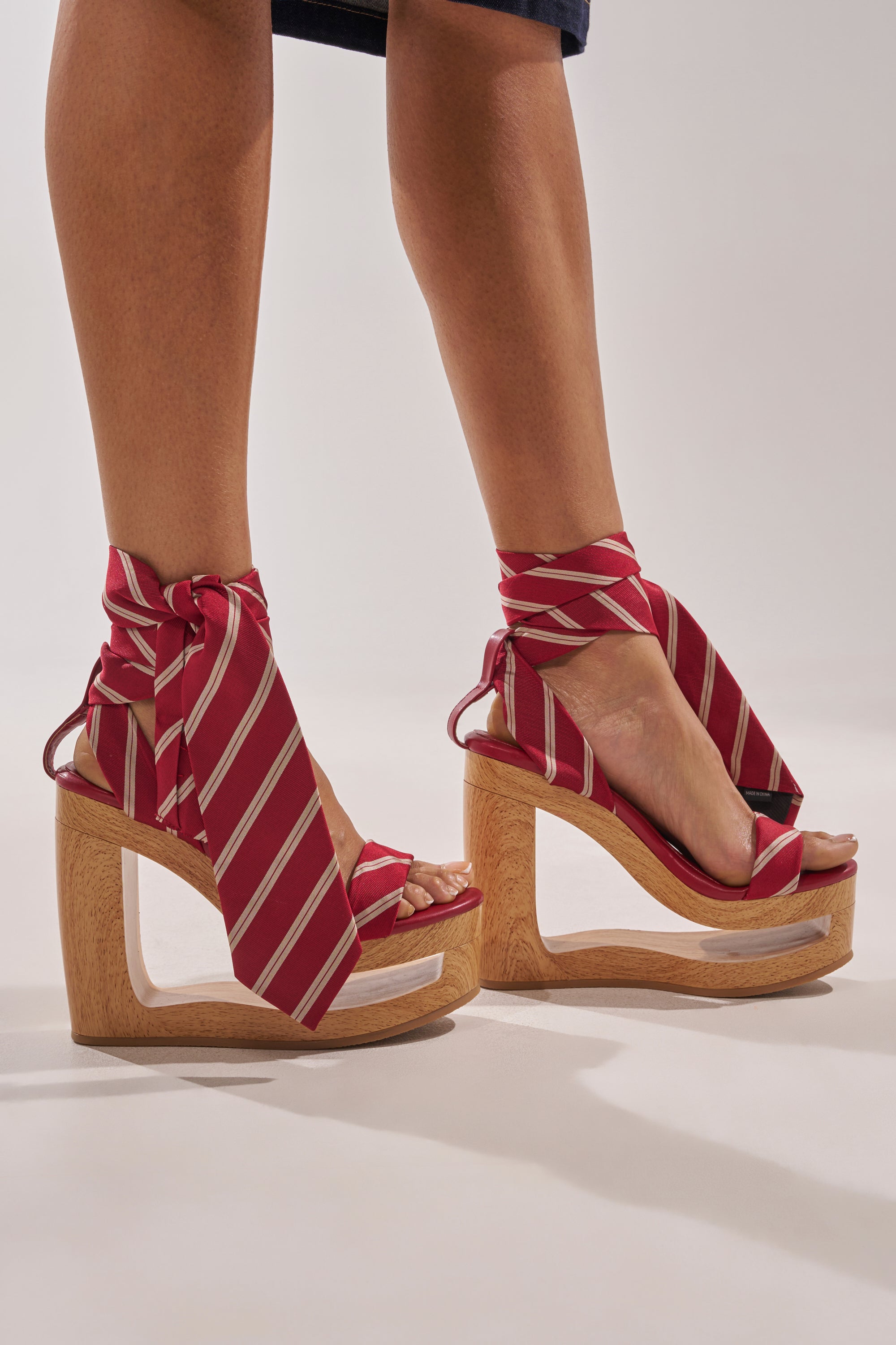 Someone stands on a neutral background wearing the AZALEA WANG WYNN RED TIE LACE UP WEDGE—unique striped tie wedge sandals with chunky wooden platform heels and red-and-white wraparound ankle ties. 0
