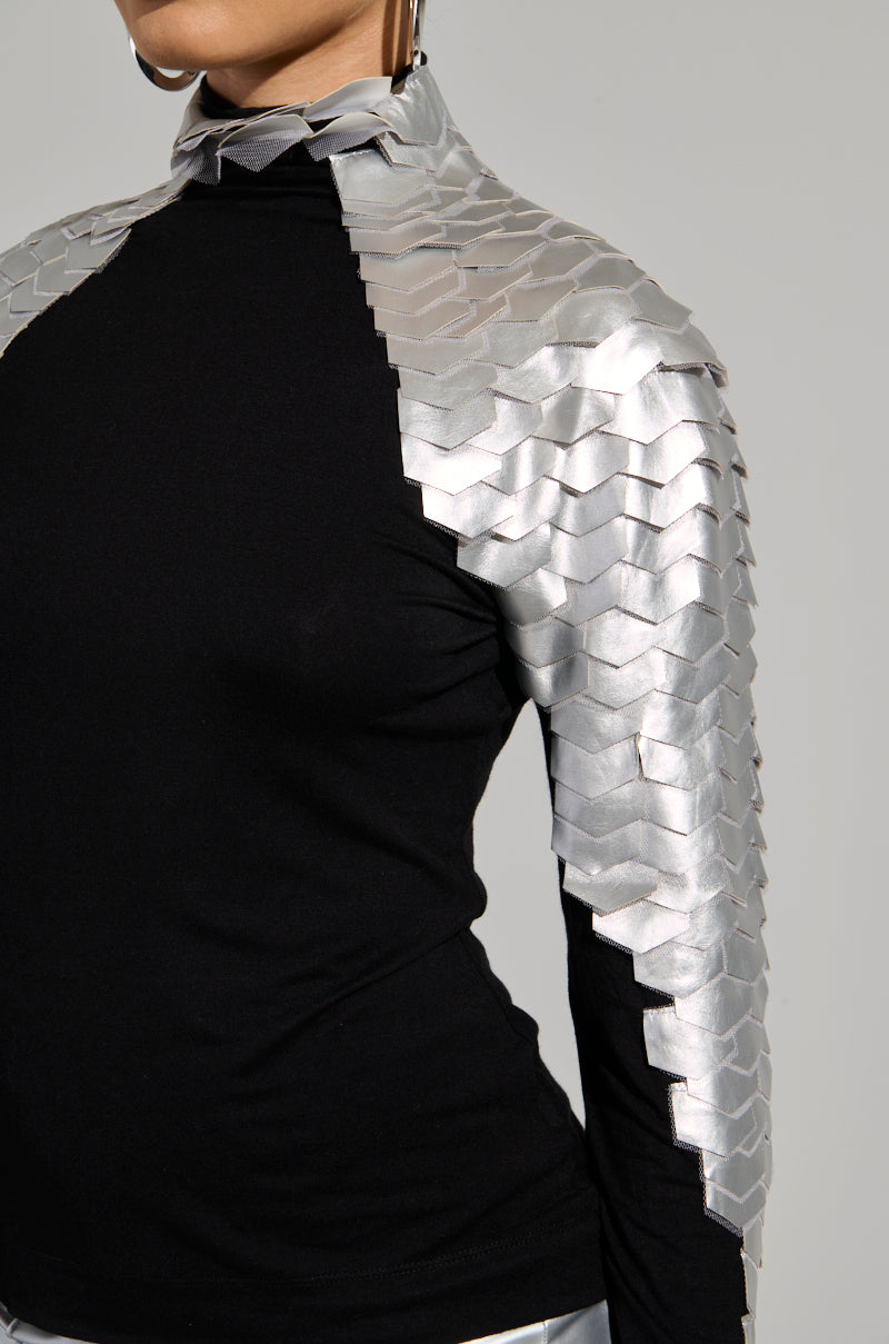 The NASTASIA 2 SCALE TOP features a chic black stretchy knit fabric adorned with metallic silver scales on the shoulders and arms, exuding a futuristic vibe. Its ruched detailing adds texture, giving it an armor-like look for a modern, edgy flair.