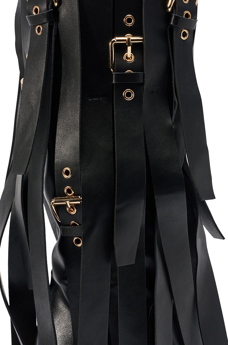 Close-up of the AZALEA WANG XANTHE BLACK BELT EMBELLISHED STILETTO BOOT shows black faux leather straps with gold buckles and eyelets, arranged vertically for a textured, layered look.
