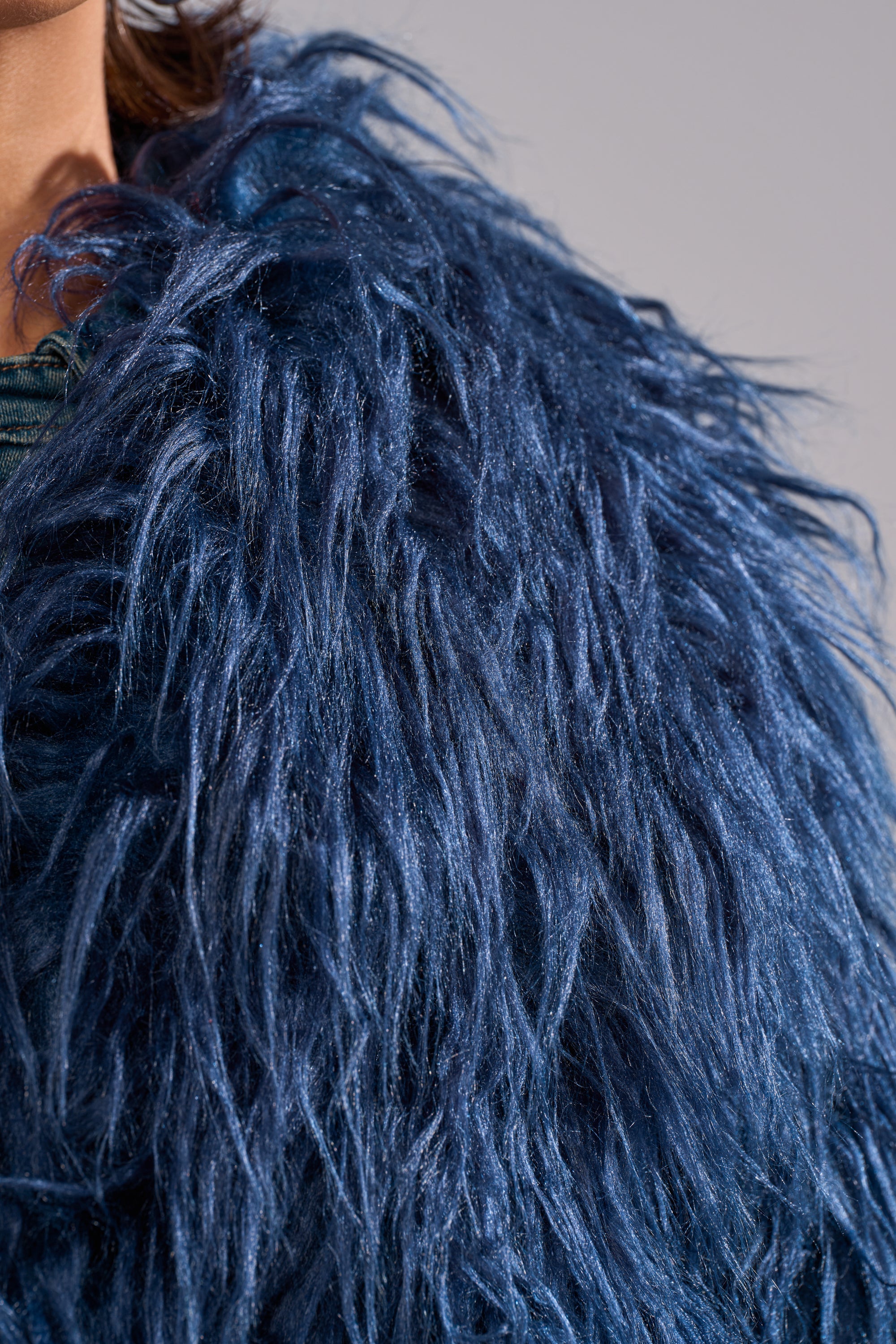 Close-up of the LIFE OF THE PARTY FAUX FUR jacket in navy blue, showcasing long, shiny strands and a glossy finish. The cropped design highlights the stylish faux fur texture with only part of the shoulder and neck visible. 10